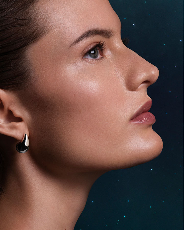 Close up of model showcasing glowing, plump skin, stood in front of a clear night sky with stars